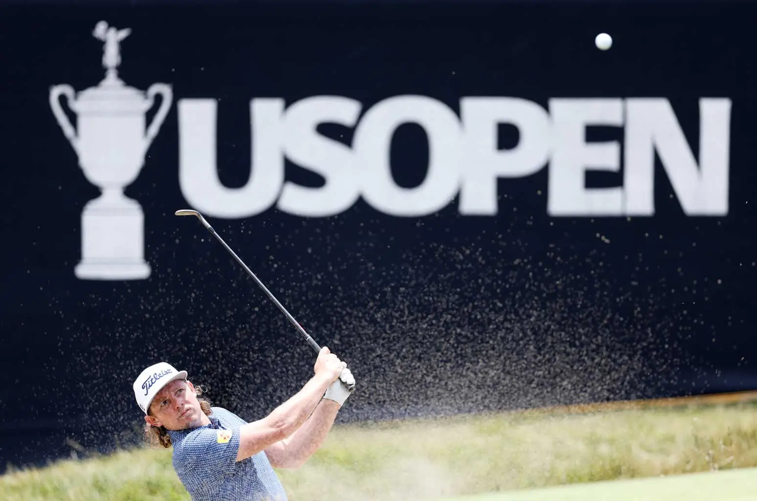 Golfer hitting bunker shot in front of giant US Open LED backdrop