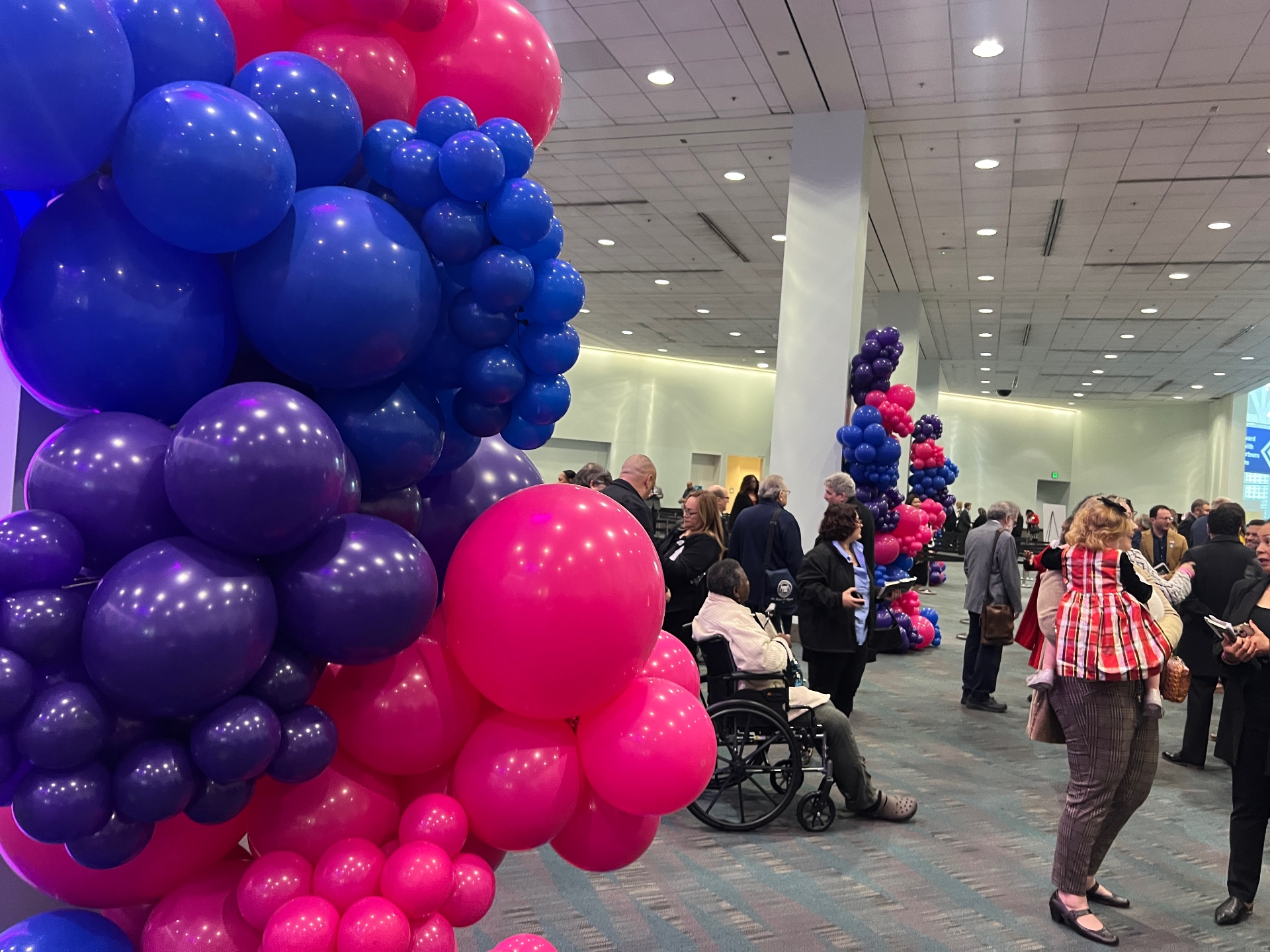 Pink, purple and blue balloon columns lining a convention center concourse during attendee arrival