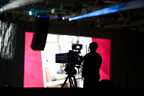 Silhouetted broadcast camera operator framing a shot against a magenta LED wall backdrop